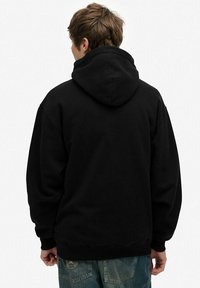 Sudadera negra con capucha de corte relajado, que presenta un bolsillo tipo canguro y puños y dobladillo de canalé. Material suave con una textura lisa.