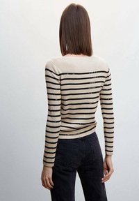 Maglione a coste con strisce orizzontali beige e nere, dal design aderente e maniche lunghe. Indossato con jeans scuri.