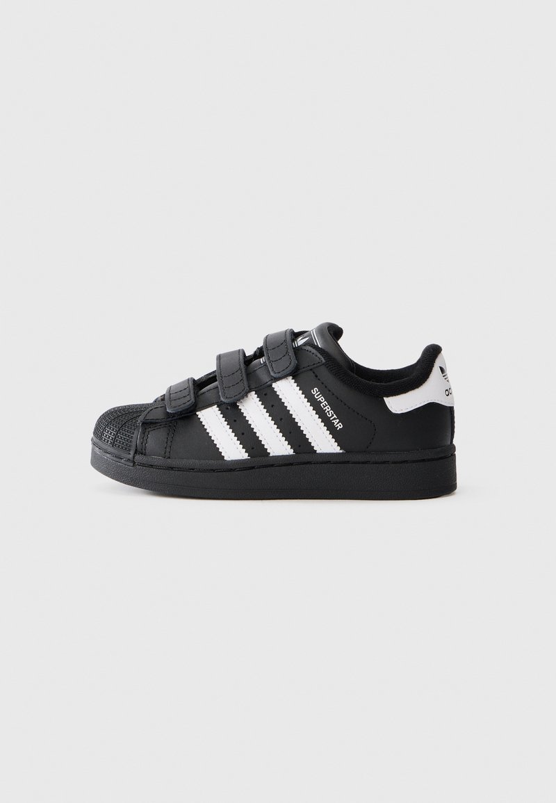 Schwarze Sneaker mit drei weißen Streifen, Gummisohle, abgerundeter Zehenpartie, strukturiertem Vorderbereich und Klettverschlüssen. Mit "Superstar"-Markierung an der Seite.