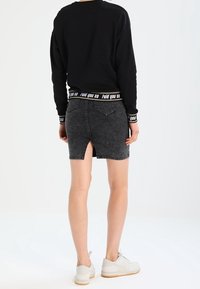 Sudadera negra con una cintura de logo acanalado, combinada con una falda de mezclilla oscura de tiro alto que cuenta con una abertura en la parte trasera. Zapatillas blancas visibles.