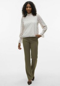Lichte, getextureerde blouse met een hoge hals en gerimpelde mouwen, gecombineerd met aansluitende olijfgroene broeken en puntige bruine schoenen.