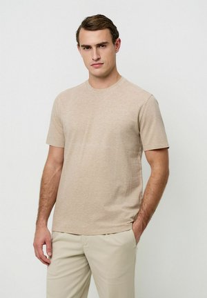 T-shirt beige a maniche corte realizzata in tessuto morbido, con scollo rotondo e vestibilità comoda. Il modello la abbina a pantaloni di colore chiaro.