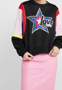 Mustat hupparit, joissa on moniväriset hihat ja iso paljettitähti muotoilu, jossa on sana "Rakkaus" paksuilla kirjaimilla. Alla vaaleanpunainen hame.