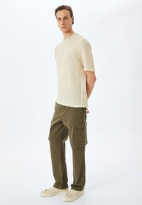 Helles Beige, gerippte Strick-T-Shirt mit kurzen Ärmeln. Kombiniert mit olivgrünen Cargo-Hosen mit zahlreichen Taschen und einer lockeren Passform.
