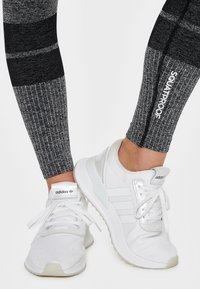 Černé a šedé legíny se vzorem a žebrovanou texturou; spárované s bílými sportovními botami s síťovaným designem a třemi proužky.