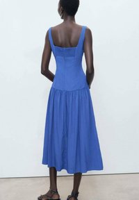 Blue cotton dress with a fitted bodice and flared skirt, featuring a textured back and wide shoulder straps.