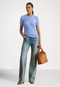 Svetlo modra kratka pulover s kablom na kratkih rokavih in okroglim izrezom, kombinirana z razširjenimi svetlimi jeans hlačami in rjavo usnjeno torbico.