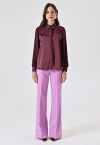 Blusa in seta borgogna con colletto e dettaglio con fiocco, abbinata a pantaloni a vita alta flared rosa pastello e décolleté a punta.