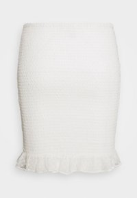 Bílá sukně se smockovanou texturou a volánkovým lemem. Vyrobena z lehké tkaniny s jemným bodovým vzorem na spodní části. Přiléhavý střih.