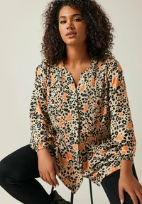Leopardmønstret bluse i beige med sorte og orange detaljer, med en plisseret front, rund udskæring og lange puffærmer.