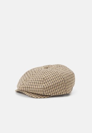 Beżowa i brązowa czapka typu flat cap w kratę, z małym daszkiem, o teksturowanej tkaninie i z okrągłym guzikiem na górze, przedstawiona na białym tle.