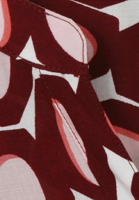 Tissu bordeaux au toucher lisse, présentant un grand motif abstrait dans des teintes de rose et de blanc. Détail de couture visible.