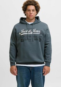 Gray hoodie with a drawstring, featuring a large print logo and text in white and black. Worn over a white shirt and paired with blue jeans.