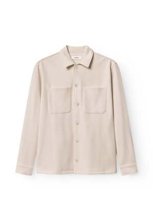 Chemise beige à manches longues en tissu texturé avec un col, deux poches avant et une fermeture à boutons. Design doux et décontracté.