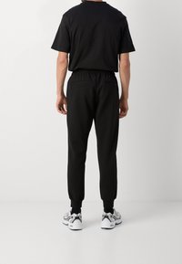 Svart kortärmad T-shirt och joggers med resårmidja och två bakfickor, tillsammans med vita träningsskor.