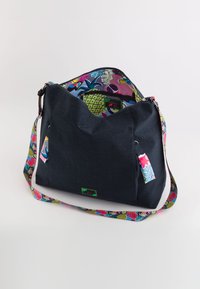 Bolsa de color azul oscuro con una abertura amplia, que cuenta con un forro de estampado colorido y un asa. Incluye una etiqueta pequeña y un exterior de tela texturizada.