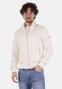 Giubbotto bomber bianco leggero con colletto alto, chiusura frontale con zip e tasche laterali. Polsini e orlo a coste con dettagli in tessuto del logo.