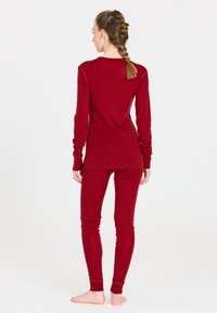 Röd långärmad topp och åtsittande leggings, tillverkade av ett mjukt texturerat material. Båda har en enkel design med långa ärmar och avsmalnande ben.