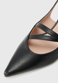 Black pointed-toe shoe made of textured leather with crisscross straps and a soft pink interior. Features a sleek, modern design.
