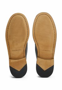 Suelas de zapatos de cuero negro con acentos de cuero color marrón claro, presentando un patrón de agarre texturizado y bordes cosidos. Logo impreso en la zona marrón.