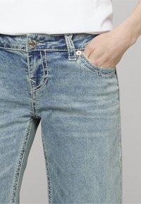 Světle modré džíny z denimu s klasickým pětipočítačovým designem, s kontrastním prošíváním a předním zapínáním na knoflík.