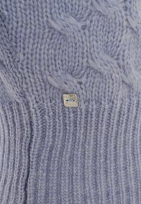 Maglione lavorato a maglia in lavanda chiaro, con una texture a coste e motivi a trecce. Un piccolo etichetta argentata è attaccata vicino al fondo.