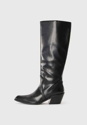 Bota de cuero negra hasta la rodilla con punta afilada, tacón angular y textura suave. Presenta un sutil acento de costura a lo largo del costado.
