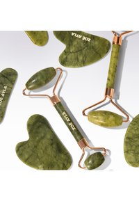 Rouleaux faciaux en jade vert et outils gua sha en forme de cœur avec des accents en or rose, disposés sur un fond blanc.