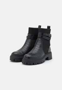 Bottes noires à la cheville en matériaux lisses et texturés. Présentent un motif crocodile, un panneau élastique et une boucle de sangle. Design à semelle épaisse.