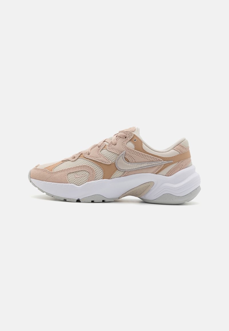 Baskets profil bas beige et rose clair avec superpositions en mesh et suède, semelle blanche épaisse et logo swoosh texturé sur le côté.