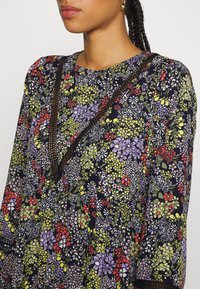 Květinové šaty s námořnickým pozadím a barevnými květy v červené, zelené a fialové. Výrazné černé lemování a strukturovaná tkanina.