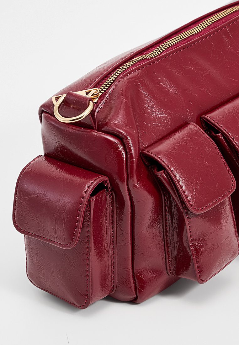 Rote Handtasche aus Kunstleder mit strukturiertem Finish, ausgestattet mit goldfarbener Hardware, einem Reißverschluss und drei Fronttaschen.