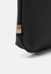 Coin de sac synthétique noir avec une surface texturée et un petit accent tissé avec des rayures beige, blanches et noires.