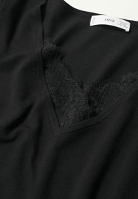 Top nero con scollatura a V realizzato in tessuto morbido, con delicati inserti in pizzo nero lungo il colletto per un tocco di texture e dettaglio.