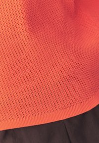 Gros plan sur un tissu tricoté orange avec un motif texturé au-dessus d'un pantalon de couleur foncée.