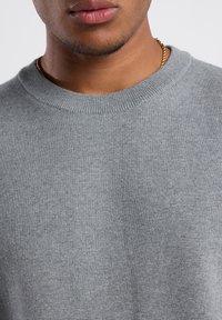 Gray knit sweater with a round neckline, textured fabric, and ribbed collar detail. Close-up view, highlighting the softness of the material.
