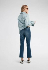 Giacca di jeans azzurro chiaro con design corto, abbinata a jeans svasati blu scuro. L'outfit è completato da scarpe in tonalità neutre.
