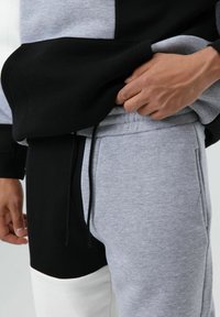 Black and gray color-blocked sweatshirt with a front pocket and drawstring. Gray sweatpants feature side pockets and a tapered fit.