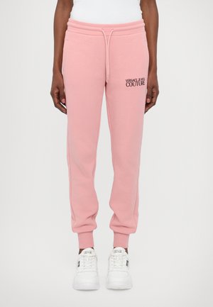 Rosa bomulls joggebukser med elastisk midje, snøring, sidelommer og logo-detaling på venstre lår. Hvite sneakers fullfører looken.