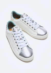 Zapatillas de cuero blancas con puntera metálica de color plata, cordones blancos y forro interior azul; cuentan con una suela texturizada y una marca en la lengua.