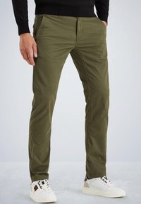 Chinos verts olive à coupe slim, avec poches avant et arrière, associés à des baskets blanches de sport. Tissu en coton, texture lisse.