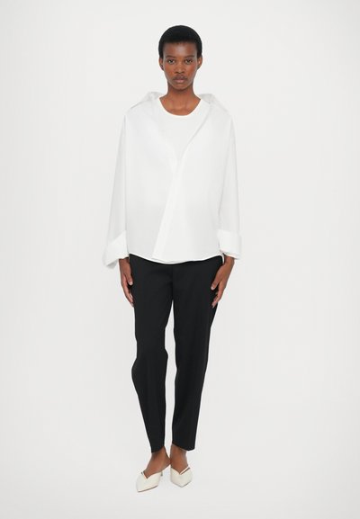 White long-sleeve button-up shirt, loose fit, paired with black tapered trousers and cream-colored pointed flats. Simple, minimal design.