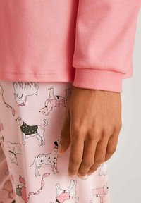 Roze langemouwen top gecombineerd met pyjama-broekjes met verschillende hondenillustraties in meerdere kleuren en patronen. Zachte stof en ribgebreide boorden.