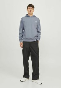 Helehall pehme hoody ees oleva tasku ja reguleeritava kapuutsiga, koos mustade cargo-pükstega, millel on mitu küljetaskut. Valged tossud.