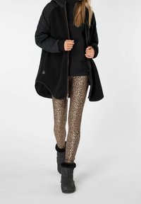 Giacca in pile nera con maniche trapuntate, dolcevita nera, leggings con stampa leopardata e stivali neri con bordino in pelliccia.