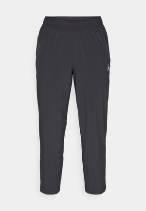 Pantalon de sport noir en tissu doux et léger avec une ceinture élastique et des chevilles resserrées, arborant un petit logo blanc sur le côté.
