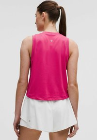 Ärmelloses rosa Sportoberteil mit atmungsaktivem Design, Netzelementen und dezentem Logo, kombiniert mit weißen Shorts.