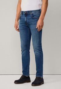 Vaqueros de mezclilla azul con un corte slim, que cuentan con un diseño tradicional de cinco bolsillos, un ligero desgaste y un cierre de botón metálico en la cintura.