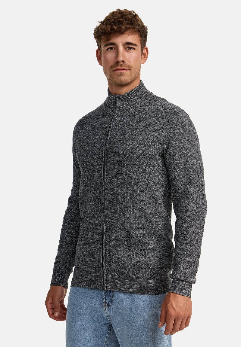 Sudadera de punto gris con cremallera, cuello alto, tejido texturizado y corte slim, combinada con pantalones de mezclilla azul claro.