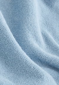 Lyseblåt tekstureret stof med en blød, lodden overflade, der har små, hævede fibre arrangeret i et glat, bølget mønster.